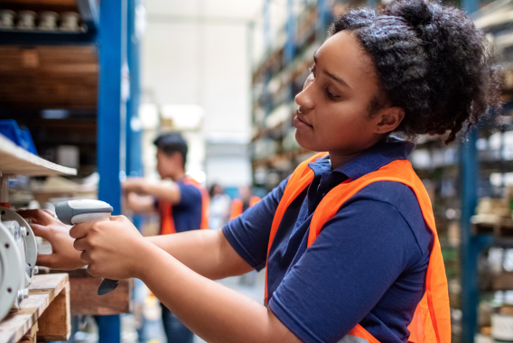 Vrouw die een product met een barcodescanner in een warehouse scant Vrouw die een product met een barcodescanner in een warehouse scant