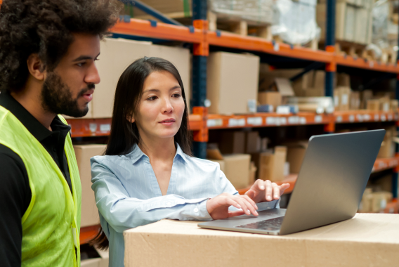 Vrouw en man die naar een laptop kijken in een warehouse Vrouw en man die naar een laptop kijken in een warehouse